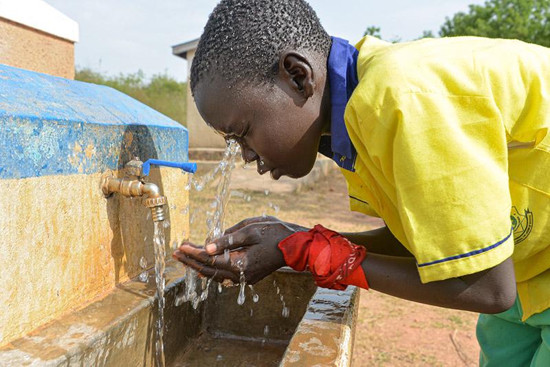 Ugandalainen poika vesihanalla pesemässä kasvojaan